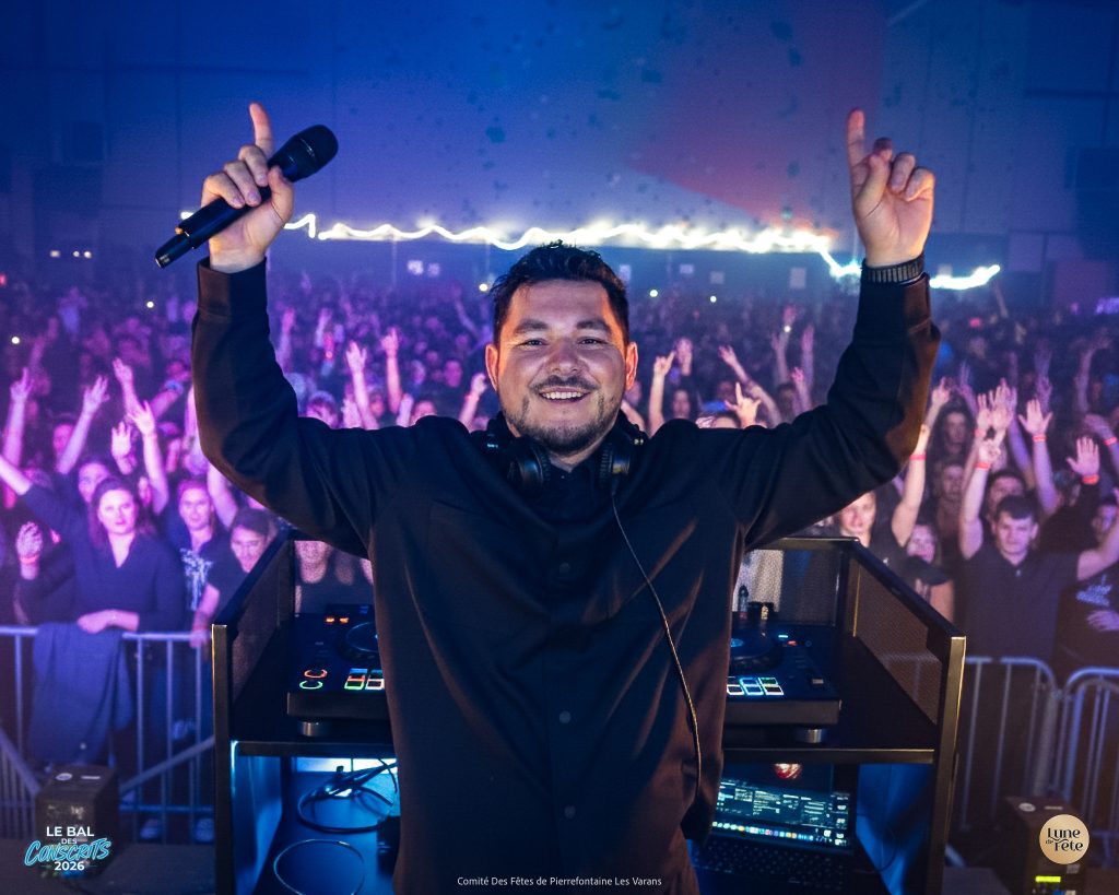 DJ Almir aux platines, tourné vers l'objectif, dos à la foule d'une soirée.